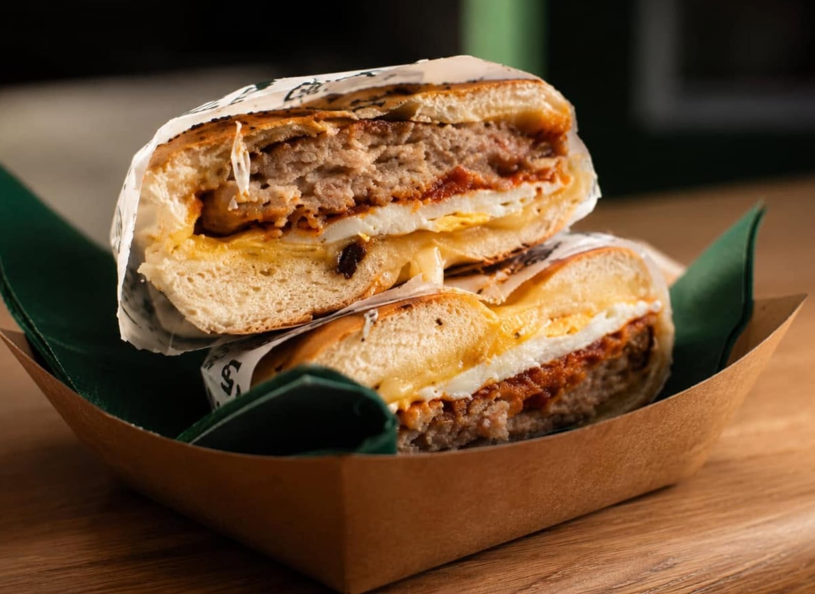 A breakfast bagel cut in half in a kraft tray — sausage patty, folded egg and melted cheddar in a toasted bagel