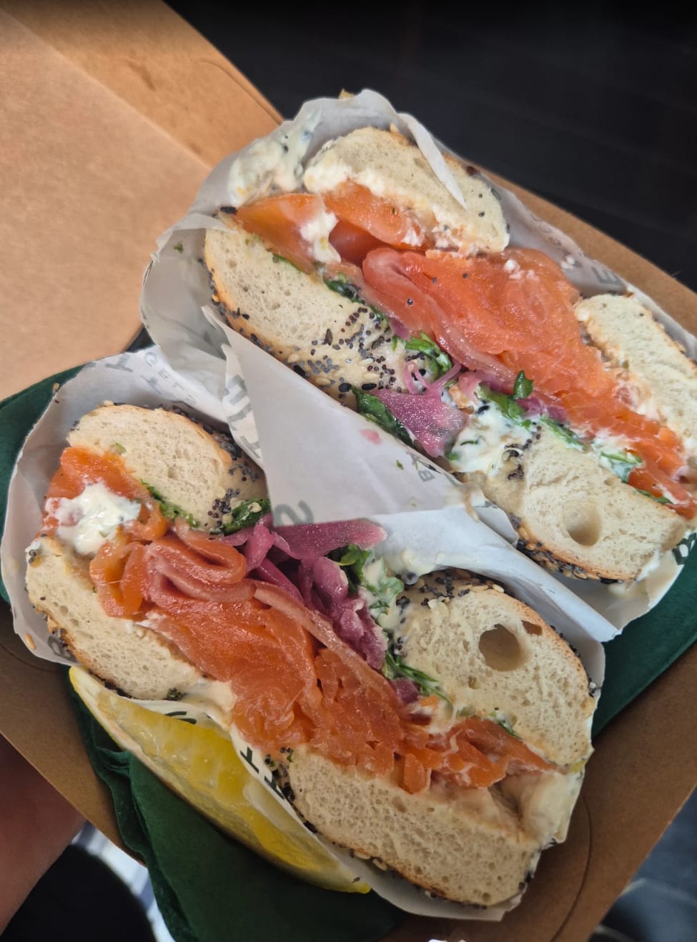 A poppy seed bagel loaded with Whitby smoked salmon, cream cheese and pickled red onion, held in a kraft tray