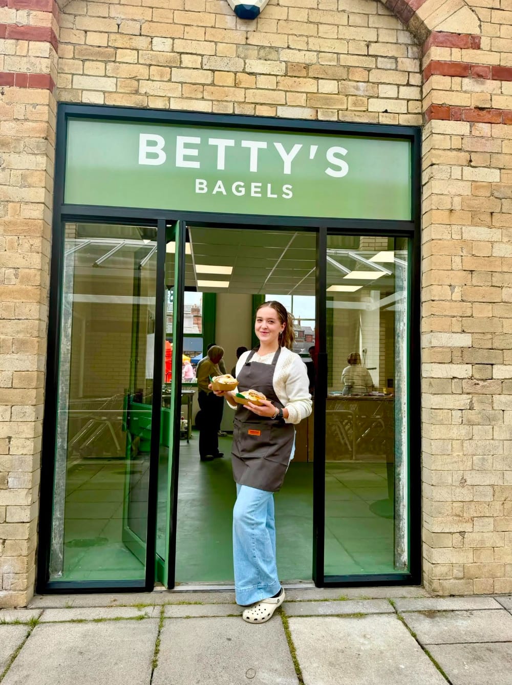 A team member holding two bagels in the doorway of Betty's Bagels on Station Square, Saltburn